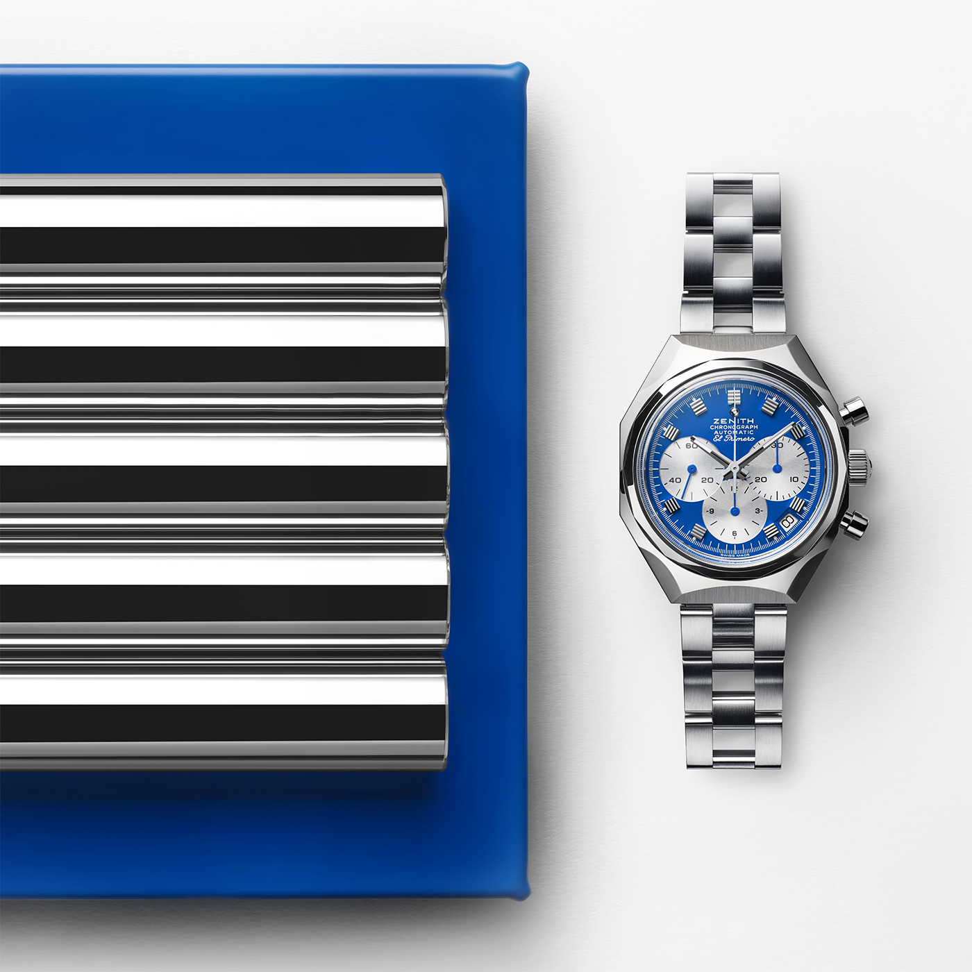 The Zenith Defy Chronograph USM - Genetian Blue, a limited edition silver timepiece with a blue and white face, is displayed next to a metallic ridged object on a blue base, set against a white background.