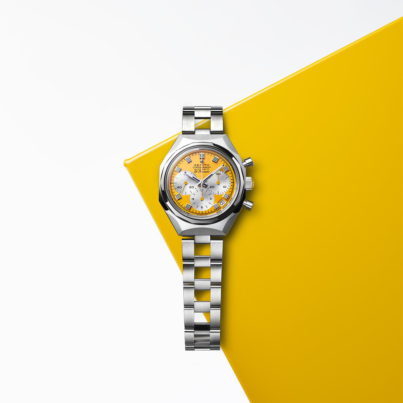 The Zenith Defy Chronograph USM - Golden Yellow by Zenith, featuring a yellow and white face, metal band, and El Primero 400 movement, rests on a yellow geometric surface against a white background.