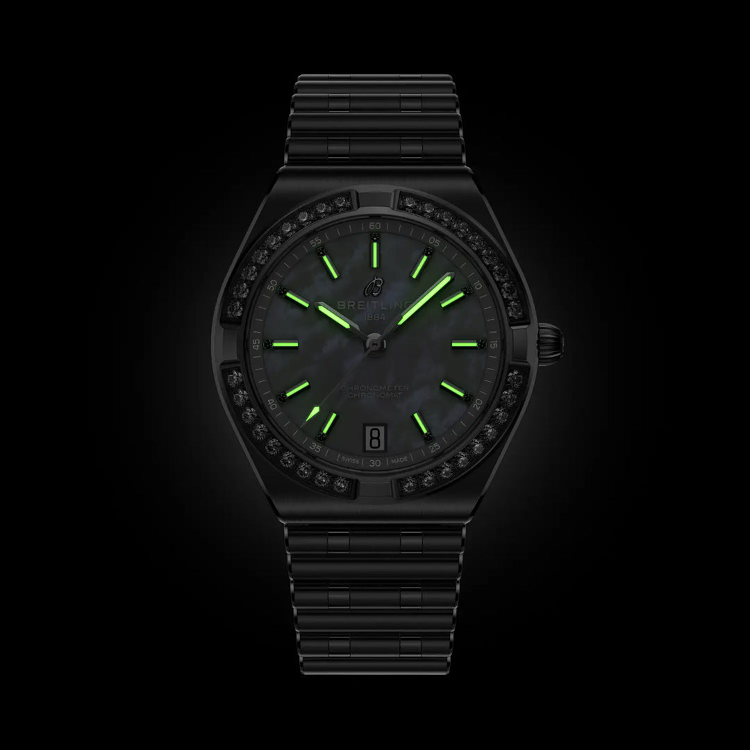The BREITLING Chronomat Automatic 36 by Breitling is a COSC-certified sports watch with a metal band, luminous green markers and hands on a dark dial, a date window at 6 o'clock, and a bezel ringed with dark stones.