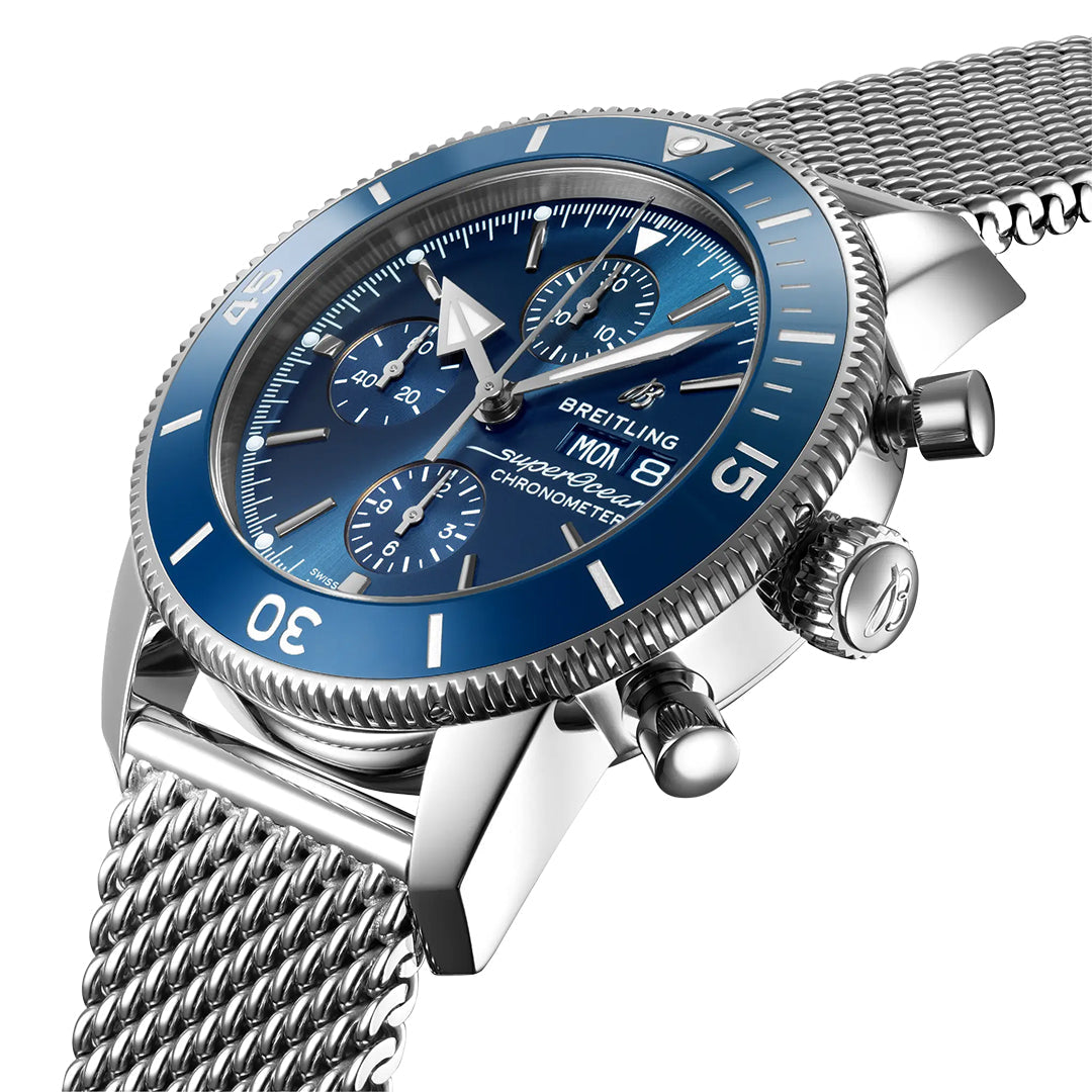 The BREITLING Superocean Heritage Chronograph 44 features a blue dial, chronograph functions, and a detailed bezel with minute markers. It includes a stainless steel mesh bracelet and is powered by Breitling Caliber 13, showcasing the day and date for the essence of a classic diver’s watch.