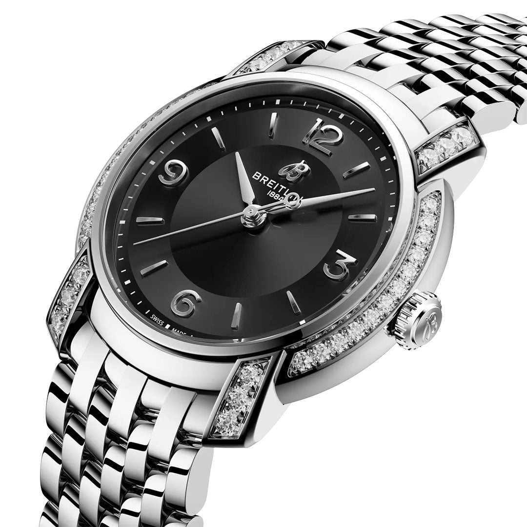 A close-up of the BREITLING Lady Premier 32 features a black dial, silver hour markers, date window, and stainless steel band. The bezel and lugs are adorned with sparkling diamonds.