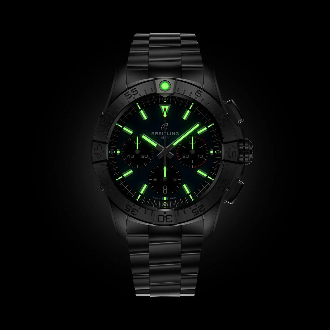 The Breitling Avenger B01 Chronograph 42 wristwatch, featuring a sleek black design with glowing green numerals and brand name, displays aviation style. Around 10:08, its metal strap and bezel stand out against the dark background with precise craftsmanship.