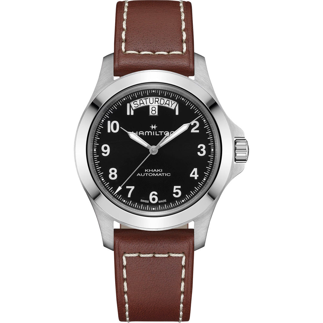 The Hamilton Khaki Field King Auto 40mm Watch by Hamilton Watch features a black dial with white numerals, day and date at 12 o'clock, silver case, and brown leather strap with white stitching.