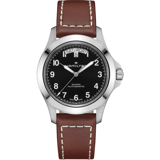 The Hamilton Khaki Field King Auto 40mm Watch by Hamilton Watch features a black dial with white numerals, day and date at 12 o'clock, silver case, and brown leather strap with white stitching.