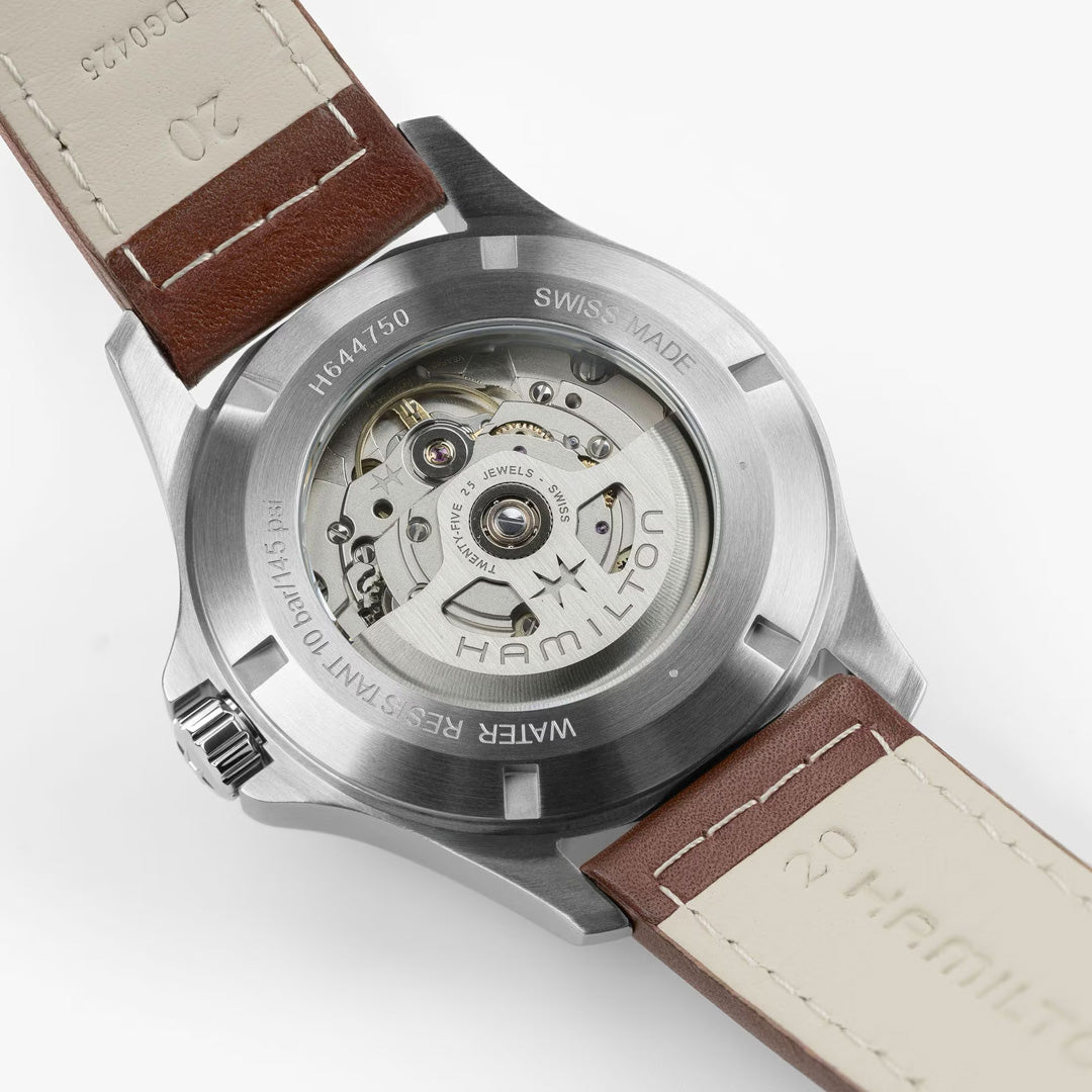Close-up of the Hamilton Khaki Field King Auto 40mm Watch by Hamilton Watch, showcasing its transparent case back with visible mechanical movement and engraved details, paired with a brown and beige leather strap.