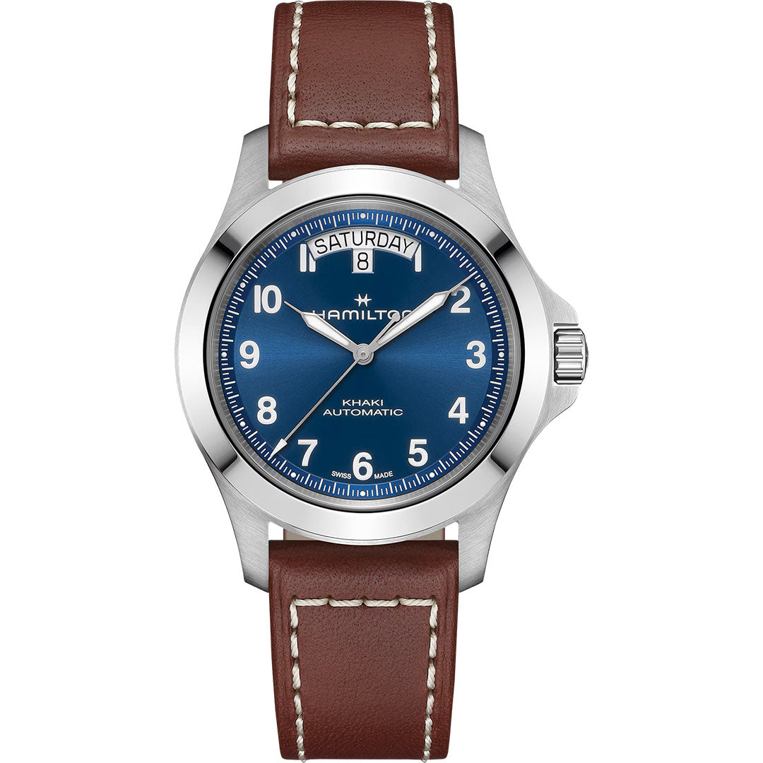 The Hamilton Khaki Field King Auto 40mm by Hamilton Watch features a blue dial, day-date at 12 o’clock, white numerals, silver bezel, and a brown leather strap with white stitching.