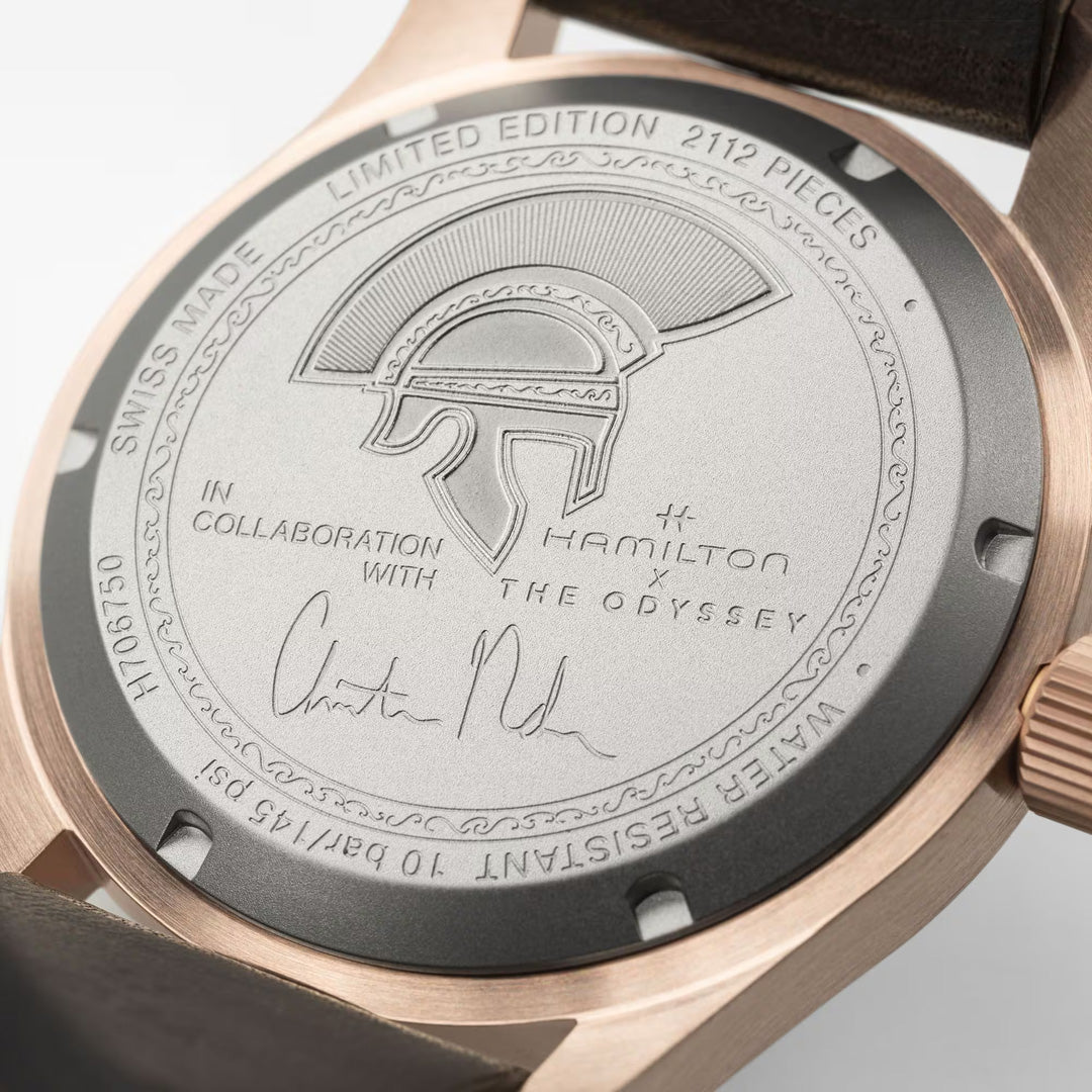 Close-up of the Hamilton Khaki Field The Odyssey Limited Edition Auto 42mm Watch case back, engraved with a helmet motif, Hamilton Watch and The Odyssey logos, “Limited Edition 2112 pieces,” and a signature. This exclusive timepiece features a brown leather strap and rose gold case—an exceptional tribute inspired by Christopher Nolan’s cinematic legacy.