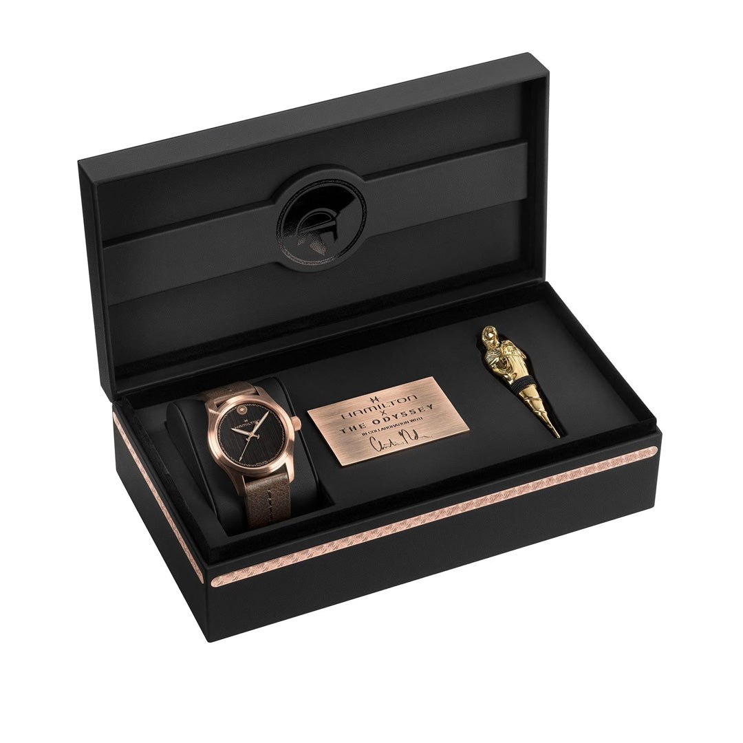 A luxurious black gift box featuring the Hamilton Khaki Field The Odyssey Limited Edition Auto 42mm Watch by Hamilton Watch, elegantly presented alongside a commemorative plaque and a gold feather-shaped pen—all meticulously arranged for an impressive presentation.