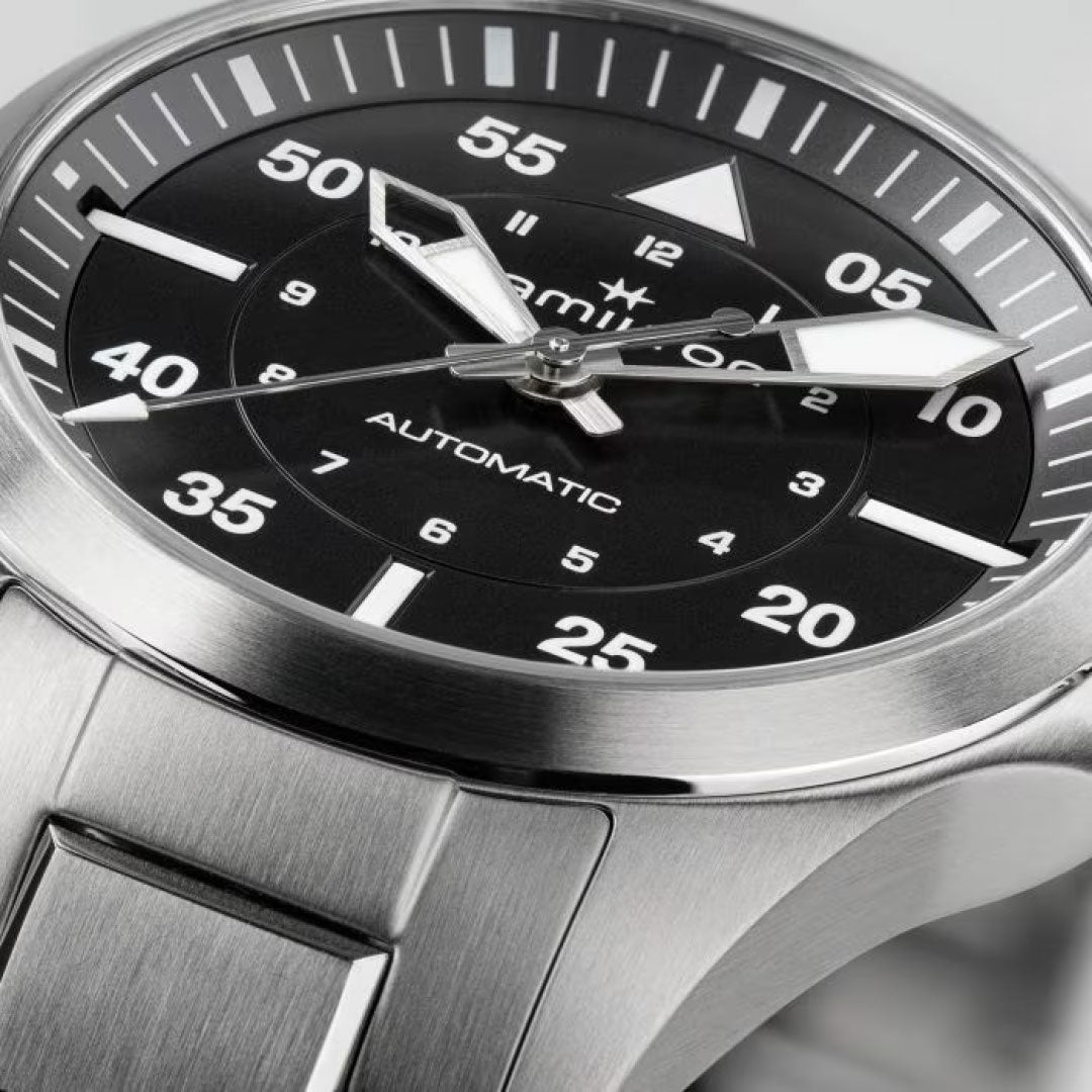 Close-up of the Hamilton Khaki Aviation Pilot Auto 36mm Watch, ideal for aviation enthusiasts. This watch by Hamilton Watch showcases a black dial adorned with bold white numerals, prominent minute markers, and three elegant hands driven by automatic movement. The bracelet is partially visible, emphasizing its polished metallic finish.