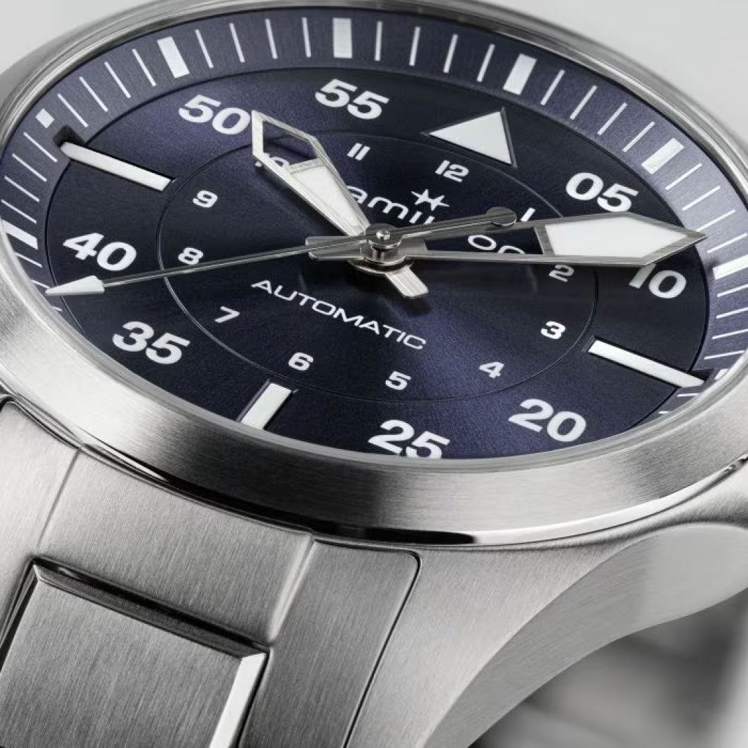 Close-up image of the Hamilton Khaki Aviation Pilot Auto 36mm Watch with a stainless-steel bracelet. The watch showcases a dark, round face adorned with bold white numerals and markings. Its hour and minute hands are silver with luminous tips. The text "Hamilton Khaki Pilot Auto" is visible alongside the word "automatic" on the watch face.