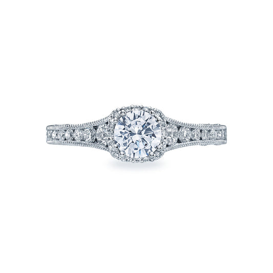 The Tacori Reverse Crescent 18K White Gold Round Brilliant Hidden Halo Diamond Engagement Ring by Tacori exudes contemporary glamour with its round central diamond encircled by smaller stones. The intricately designed band is adorned with additional tiny diamonds, creating the stunning appearance of a diamond crown on your finger.