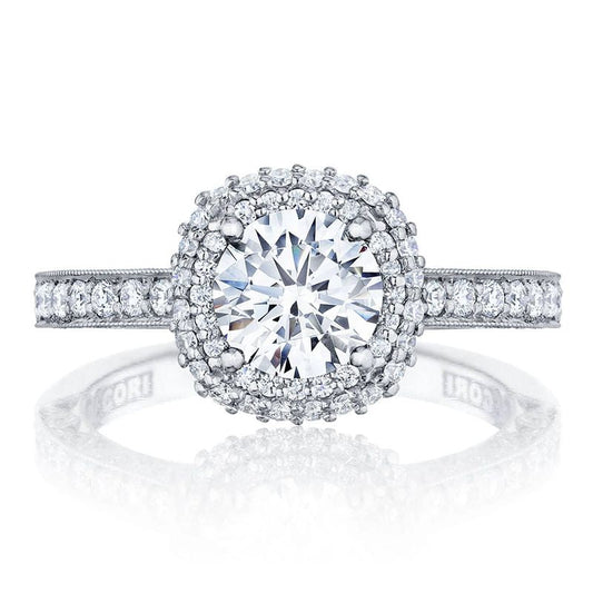 An 18K white gold Tacori Classic Crescent engagement ring showcases a prominent round brilliant diamond at the center, surrounded by smaller diamonds in a halo setting. The band features Signature Crescent detailing adorned with tiny gemstones and is engraved inside with "TACORI.