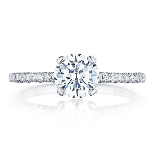 The Tacori Petite Crescent 18K White Gold Round Brilliant Solitaire Semi Mount with Diamond Band Engagement Ring highlights a large round-cut center diamond, accompanied by smaller diamonds in the Petite Crescent arrangement along the band. This stunning engagement ring is displayed against a plain white backdrop, emphasizing its brilliance and detailed craftsmanship.