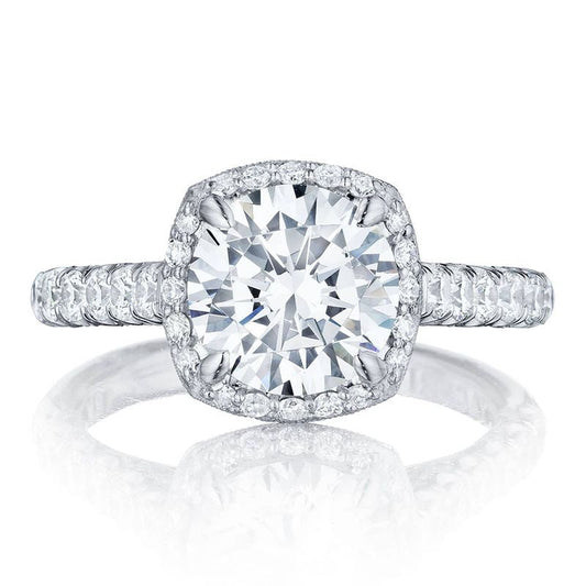 The Tacori Petite Crescent Platinum Cushion Semi Mount Engagement Ring features a stunning close-up of its large center diamond encircled by a halo of smaller diamonds. This Tacori masterpiece has a band adorned with pave diamonds, accentuating the cathedral foundation's sparkle and brilliance.
