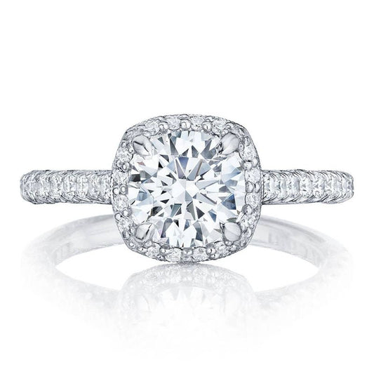 A Tacori Petite Crescent engagement ring in 18K white gold featuring a cushion semi-mount design, highlighted by a diamond halo with smaller diamonds, and a band embellished with additional small diamonds.