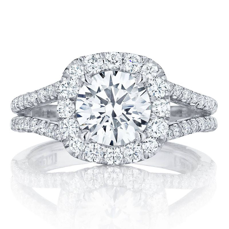 The Tacori Petite Crescent 18K White Gold Cushion Semi Mount Engagement Ring showcases a prominent central stone encircled by a dazzling diamond halo. Its cathedral-inspired band is elegantly split into dual rows, embellished with additional diamonds, offering a luxurious sparkle crafted by Tacori gemologists.