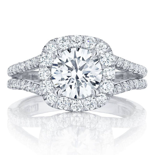 The Tacori Petite Crescent 18K White Gold Cushion Semi Mount Engagement Ring showcases a prominent central stone encircled by a dazzling diamond halo. Its cathedral-inspired band is elegantly split into dual rows, embellished with additional diamonds, offering a luxurious sparkle crafted by Tacori gemologists.