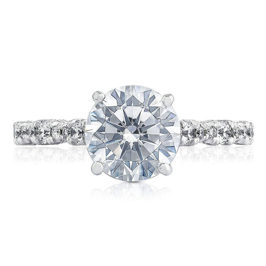 A close-up of the Tacori Petite Crescent engagement ring highlights a stunning round brilliant center diamond, beautifully complemented by a diamond band, all set in an elegant 18K white gold setting with a Cathedral foundation.