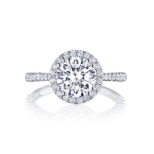 The Tacori Petite Crescent 18K White Gold Round Brilliant Semi Mount with Diamond Band and Halo Engagement Ring showcases a round central diamond encircled by a halo of smaller diamonds. Crafted with precision, the band is adorned with additional diamonds, enhancing the ring's sparkle and elegance.