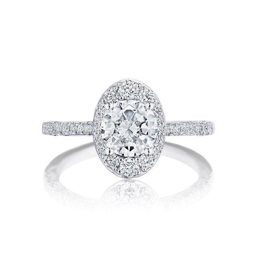 This elegant Tacori Petite Crescent engagement ring in 18K white gold showcases a stunning round brilliant diamond at the center, encircled by a halo of smaller diamonds. The band, crafted by Tacori gemologists, features delicate diamonds and a crescent design embellished with additional diamonds for an opulent and sparkling look.