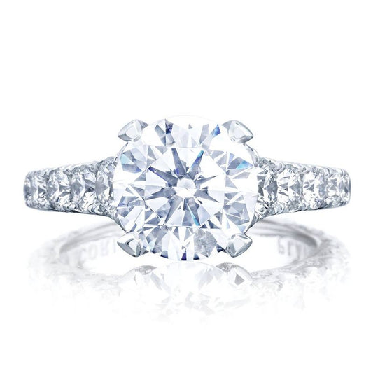 The Tacori Petite Crescent RoyalT Platinum Round Brilliant Solitaire Semi Mount Engagement Ring showcases a prominent round center stone in a classic prong setting. The elegantly designed band, featuring Tacori's signature hidden bloom pattern, is adorned with smaller diamonds, offering an exquisite look. Set against a white background, this piece from Tacori exudes timeless beauty.