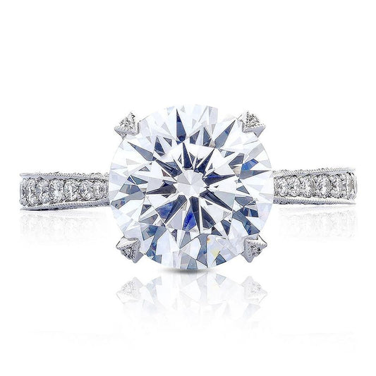 A close-up of the Tacori Classic Crescent RoyalT Round Brilliant Solitaire Semi Mount with Diamond Band Engagement Ring highlights a prominent round-brilliant diamond at its center, elegantly set on a band adorned with smaller diamonds. The design includes four prongs securing the central diamond, meticulously crafted by TACORI gemologists.