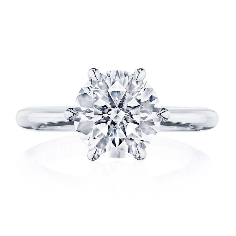 A close-up of the Tacori Founder's Collection RoyalT Platinum engagement ring showcases a round brilliant solitaire diamond set on a simple, polished band. The diamond is prominently featured and sparkling against a white background, reflecting Tacori's exquisite craftsmanship.