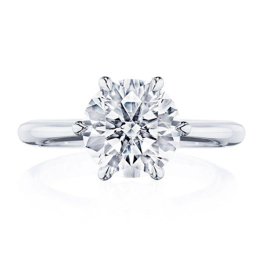 A close-up of the Tacori Founder's Collection RoyalT Platinum engagement ring showcases a round brilliant solitaire diamond set on a simple, polished band. The diamond is prominently featured and sparkling against a white background, reflecting Tacori's exquisite craftsmanship.