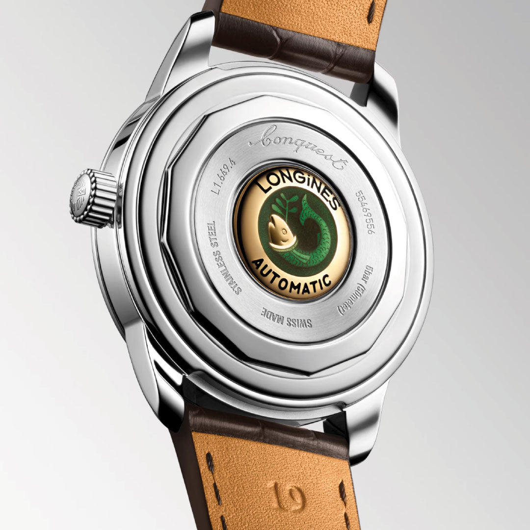 Close-up of the Longines Conquest Heritage Automatic 38mm shows a transparent caseback with logo, green medallion, engraved text, and a brown leather strap—blending vintage charm with modern craftsmanship.