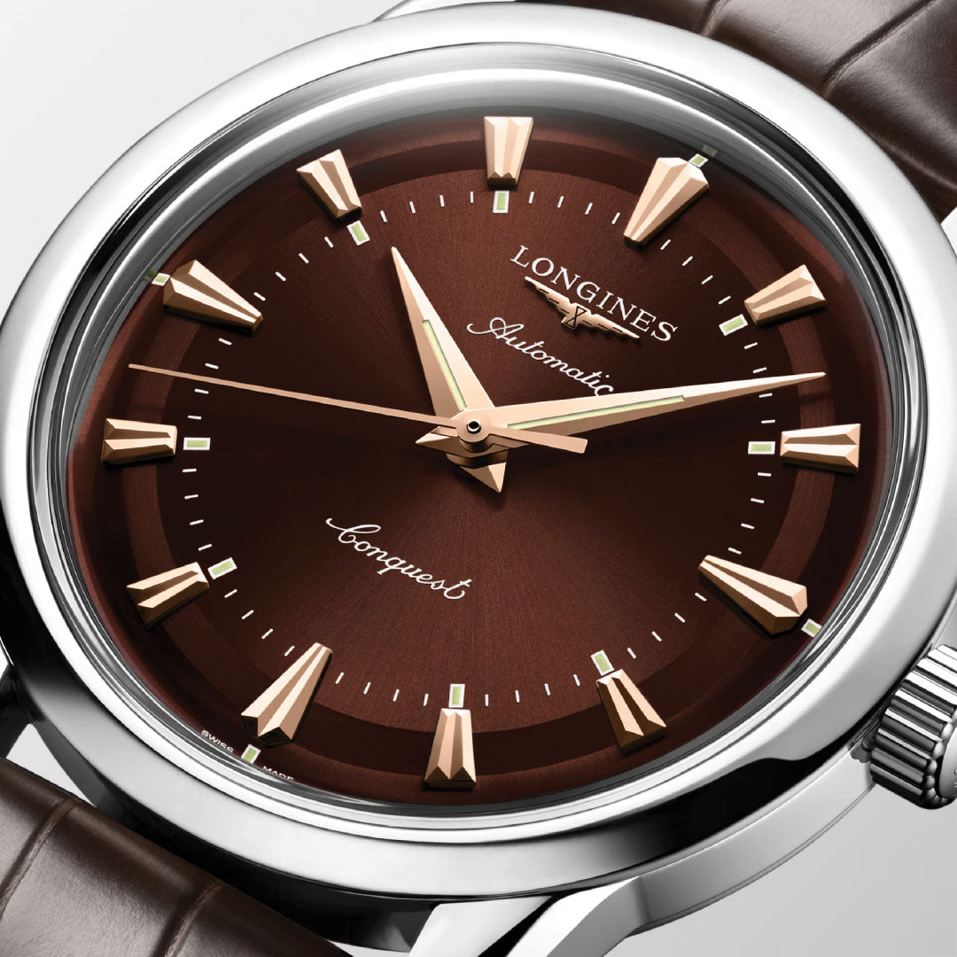 A close-up of the Longines Conquest Heritage Automatic 38mm Watch highlights its brown sunburst dial, gold markers and hands, polished silver case, and brown leather strap—showcasing Longines' timeless vintage design.