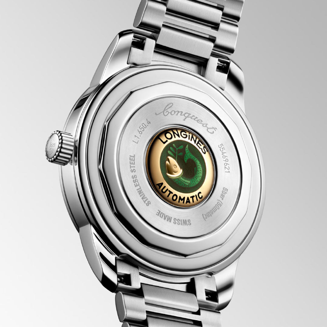 Close-up of the Longines Conquest Heritage Automatic 40mm Watch displays its vintage-inspired design, transparent caseback, gold and green emblem, stainless steel casing, and engraved details from Longines.