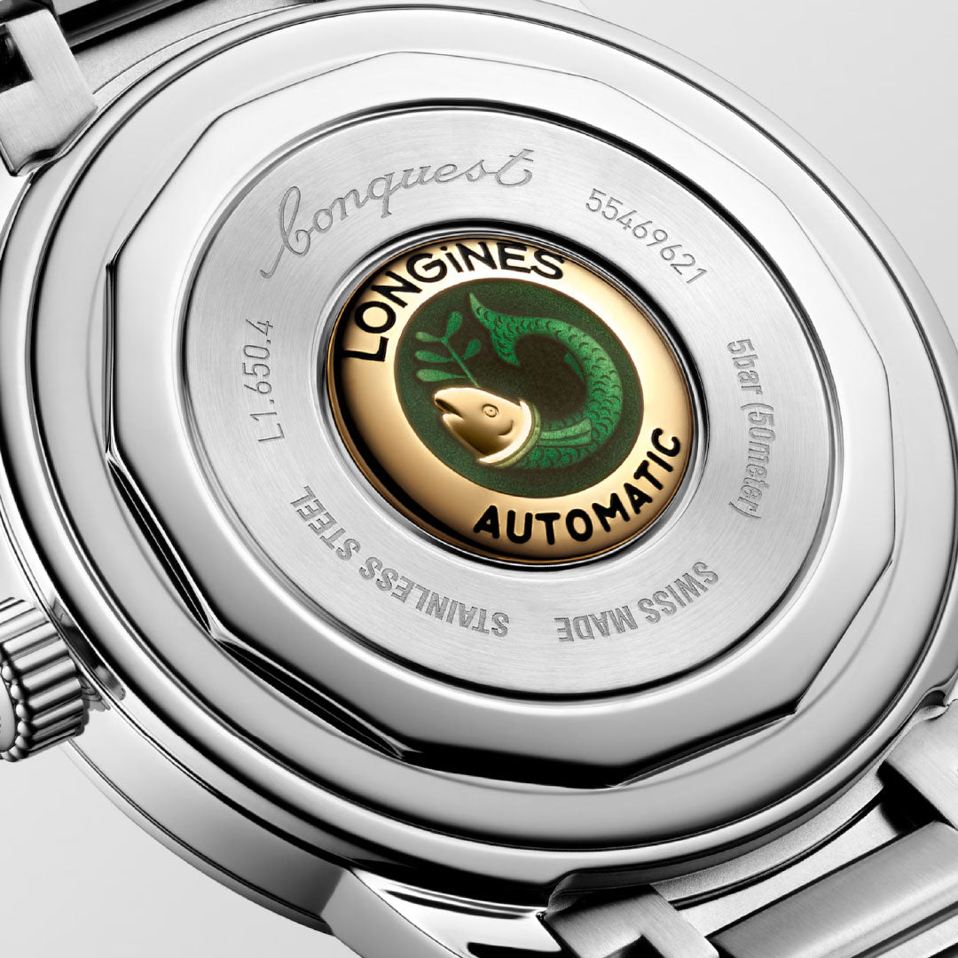Close-up of the Longines Conquest Heritage Automatic 40mm Watch, showcasing its vintage-style engraved stainless steel case back and gold medallion with a green fish logo at the center.