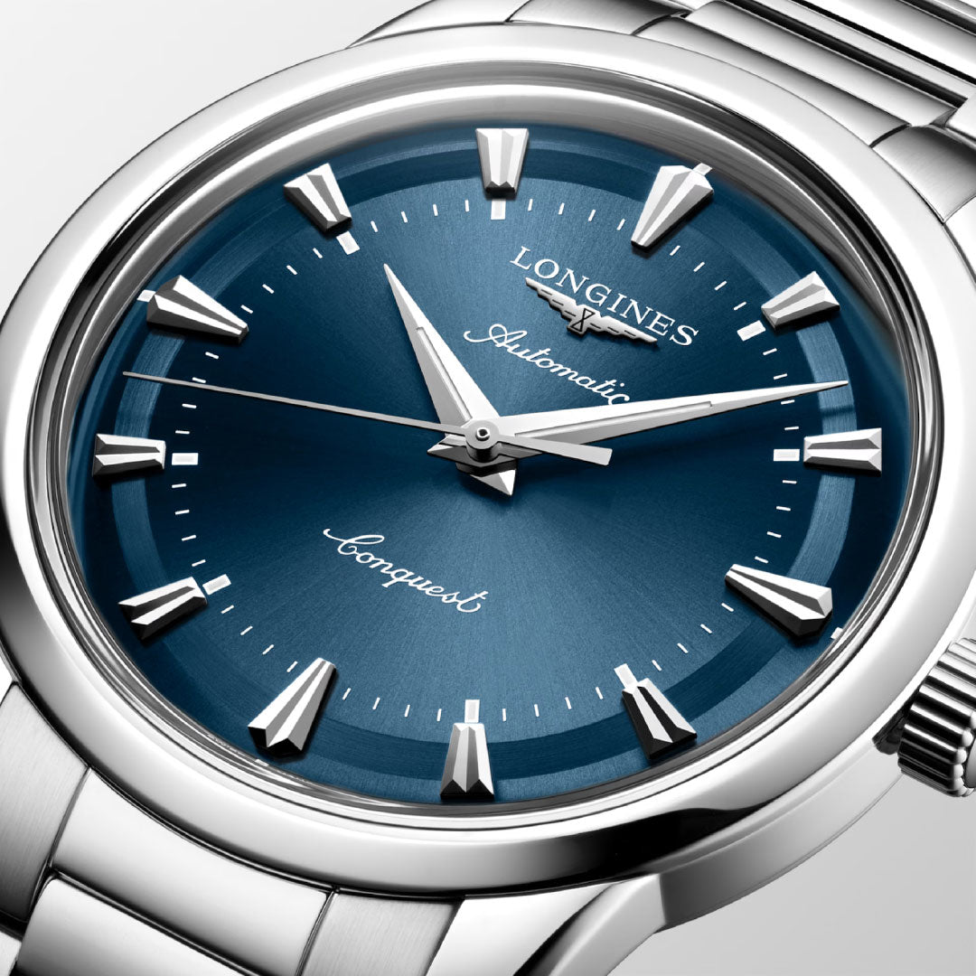 A close-up of the Longines Conquest Heritage Automatic 40mm Watch, featuring a metallic blue dial, silver hour markers, and a stainless steel bracelet, inspired by the vintage designs of Longines’ classic Heritage collection.