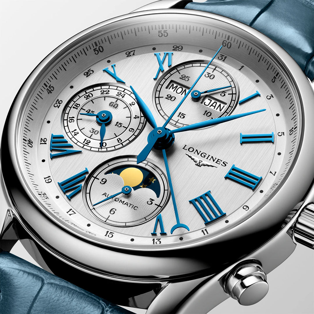 Close-up of the Longines Master Collection Automatic Moonphase 40mm Watch, featuring a silver dial, blue Roman numerals and hands, three subdials for day, date, and moon phase, plus a blue leather strap by Longines.