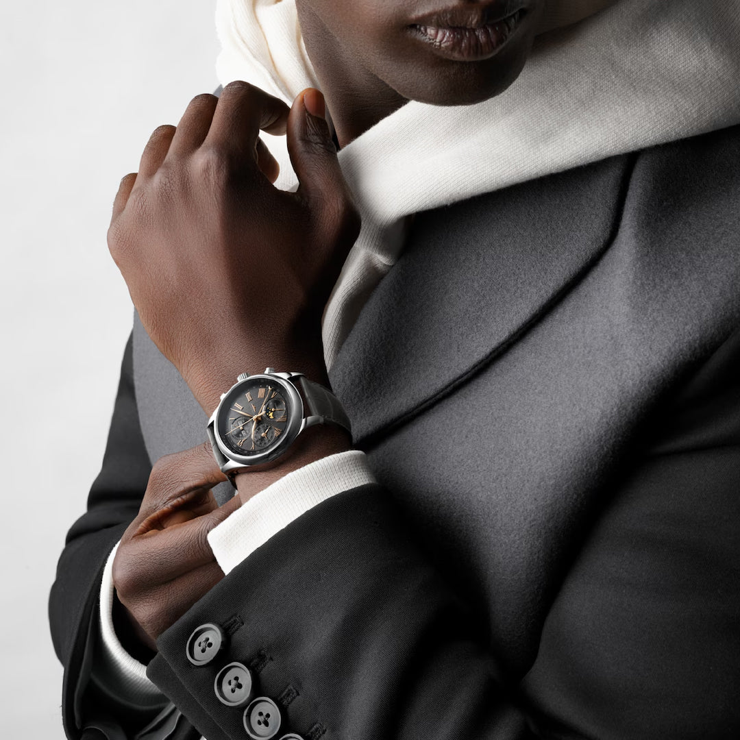 Dressed in a dark suit and white hoodie, a person displays the Longines Master Collection Chrono Moonphase Automatic 42mm watch prominently on their left wrist, highlighting its intricate dial and exquisite craftsmanship.