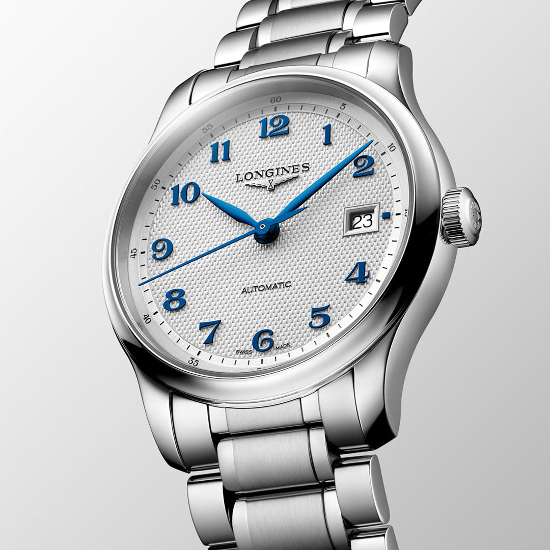 The Longines Master Collection Automatic 39mm Watch, crafted in silver by the esteemed brand Longines, displays a white textured dial complemented by blue hands and numerals, a date window at 3 o’clock, and a sleek metal bracelet—gracefully photographed at an angle on a light background and embodying the finest in Swiss watchmaking tradition.