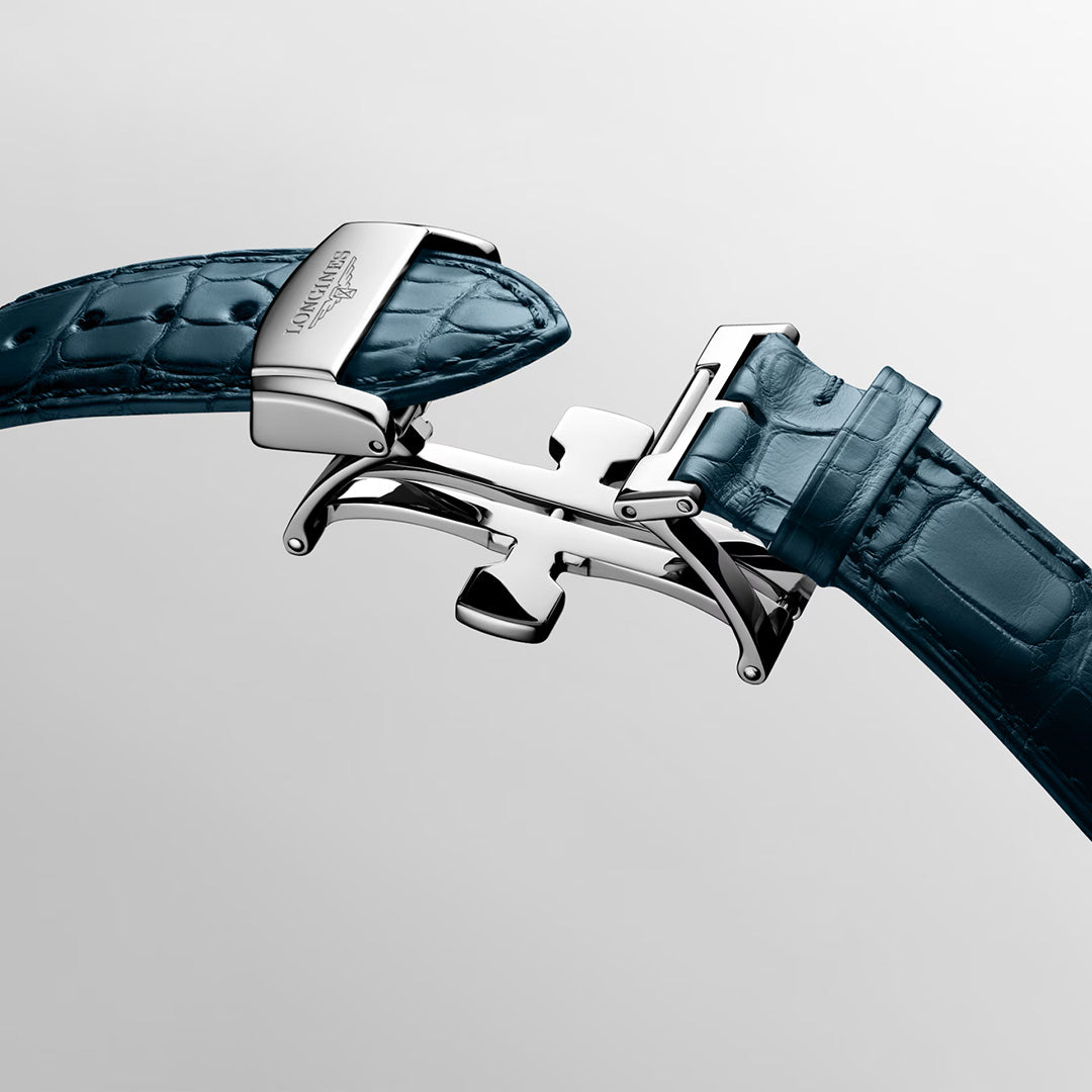 A close-up of a silver clasp on a blue crocodile-pattern leather watch strap showcases the intricate deployment buckle mechanism—an exquisite detail that exemplifies the fine craftsmanship of the Longines Master Collection Automatic 41mm Watch by Longines.