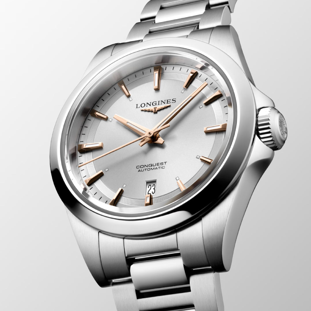 A close-up of the Longines Conquest Automatic 30mm Watch, an ideal choice for daily wear, features a silver stainless steel bracelet, a white dial, gold-tone hour markers and hands, and a date window at 3 o'clock, all set against a light gray background.