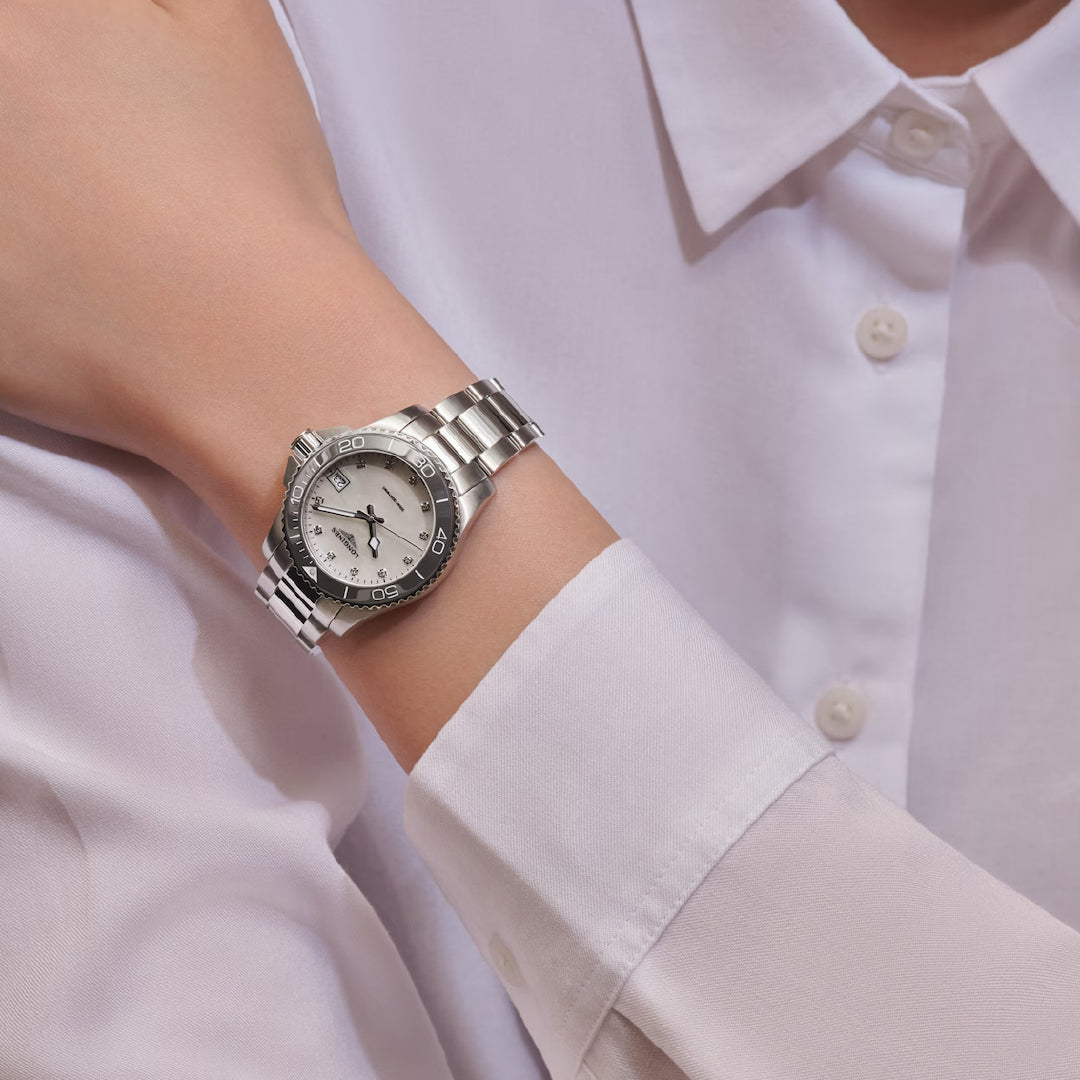A person wearing a Longines HydroConquest Quartz 32mm Watch with a silver strap, white dial, hour markers, and date display rests their hand on their wrist while dressed in a crisp white shirt.