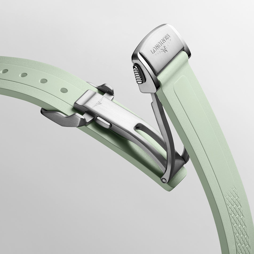 The image highlights the mint green watch strap of the Longines Conquest Automatic 34mm Watch, featuring a silver deployment clasp that exemplifies horological excellence. The clasp is engraved with the Longines logo and adorned with textured details, all set against a plain white background.