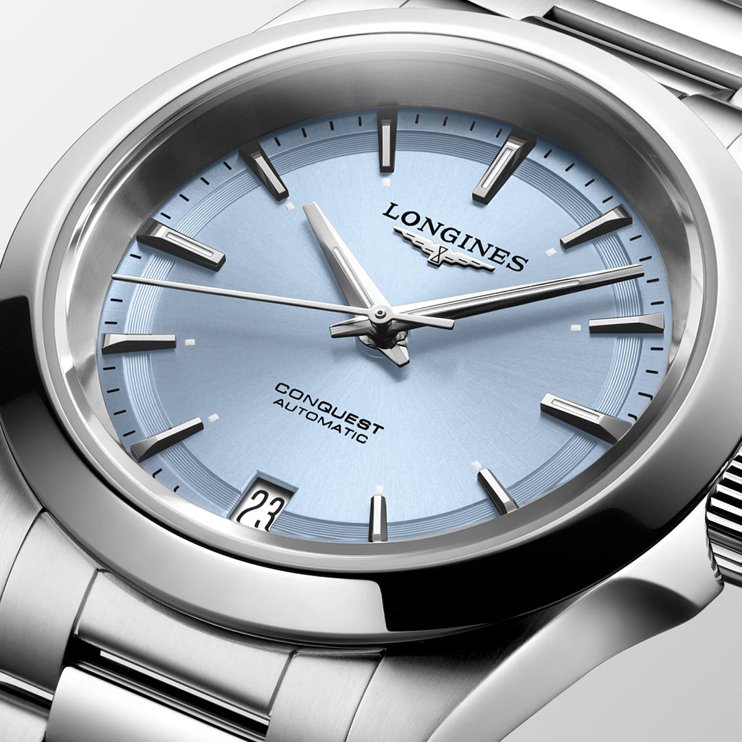 Close-up of a stunning Longines Conquest Automatic 34mm watch featuring a light blue face. The timepiece, branded as "Longines Conquest Automatic," boasts elegant silver hour markers and a date display at 3 o'clock, beautifully arranged on a shiny metal bracelet.