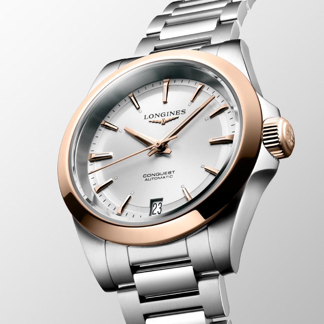 The Longines Conquest Automatic 34mm watch exemplifies horological excellence, featuring a sophisticated silver and rose gold design with a date display positioned at 6 o'clock. Its metallic strap is elegantly presented against a subtle gradient background, highlighting its exquisite craftsmanship.