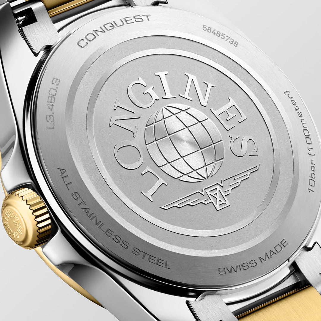 Close-up of a silver-toned Longines Conquest Quartz 34mm Watch case back featuring an engraved globe logo, winged hourglass, and technical specifications, with a gold-toned crown on the left.