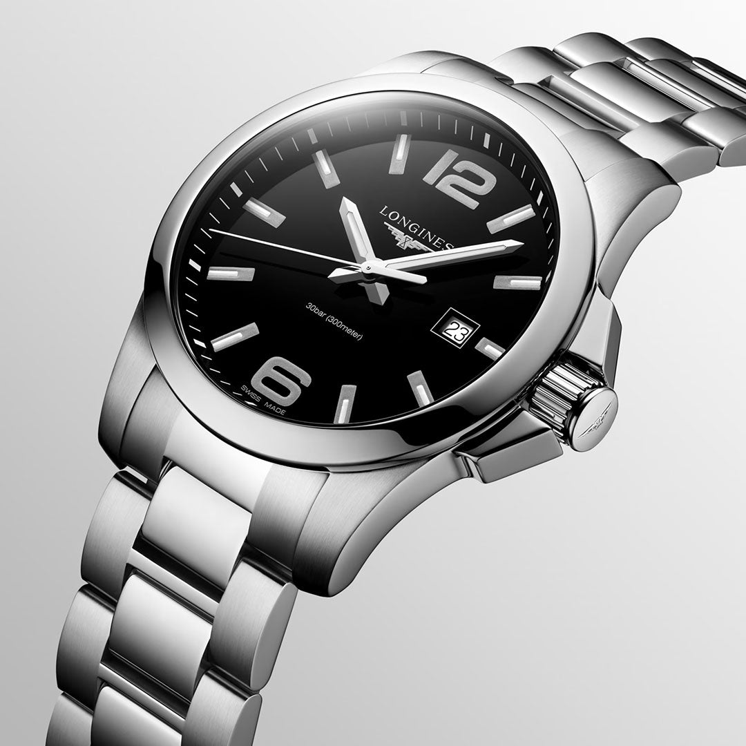 A close-up of the Longines Conquest Quartz 43mm Watch showcases its silver case, black dial with silver markers, and date at 3 o’clock on a matching bracelet—sporty elegance from Longines for everyday wear.