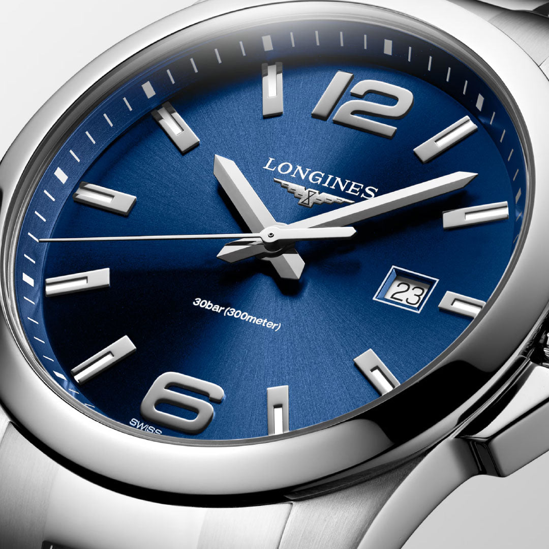 Close-up of a Longines Conquest Quartz 43mm stainless steel watch featuring a blue dial, silver markers and hands, date window at 3 o’clock, and water resistance to 30 bar (300 meters). Brand: Longines.