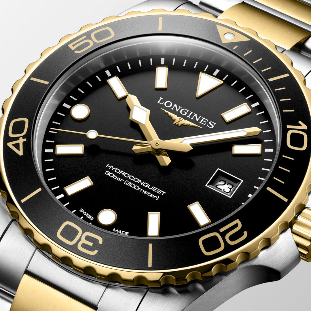 A close-up of the Longines HydroConquest Quartz 42mm Watch highlights the precision of Swiss watchmaking, featuring a striking black and gold bezel, black dial, gold markers and hands, date display, and a two-tone metal bracelet—an elegant addition to Longines’ renowned sport watch collection.