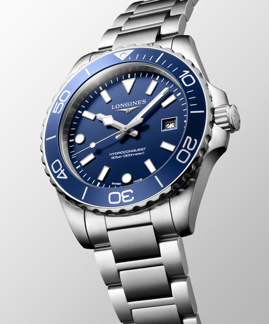 A Longines HydroConquest Quartz 42mm Watch by Longines, featuring a silver stainless steel case and metal bracelet, a blue dial and bezel, white hour markers, and a date window at 3 o’clock, is displayed at an angle against a light gray background.