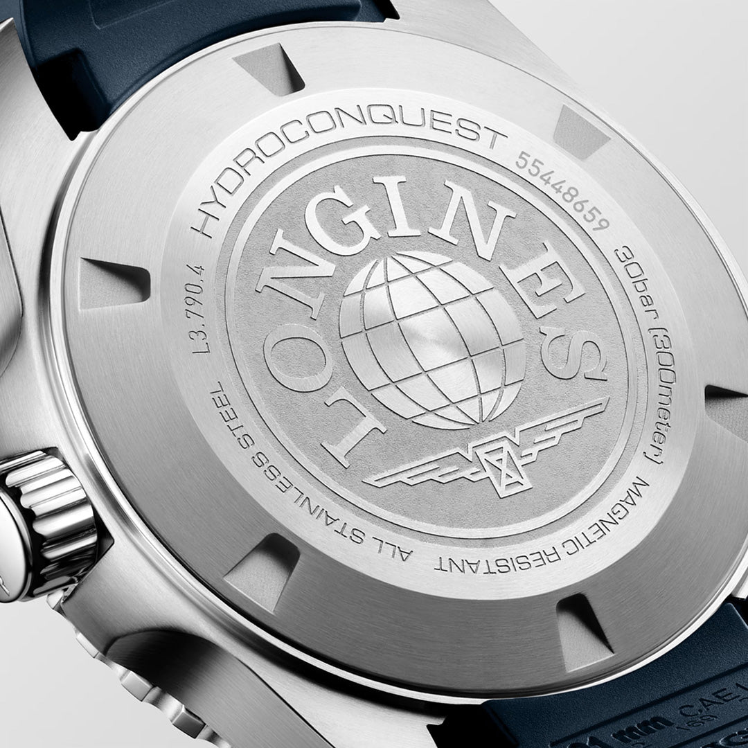 Close-up of the back of the Longines HydroConquest GMT Automatic 41mm Watch by Longines, part of the Sport Collection, showcasing engraved branding, a globe logo, water resistance rating, and specifications about stainless steel and magnetism resistance. A navy blue strap is partially visible. Swiss Super-LumiNova enhances legibility while complementing its robust design.