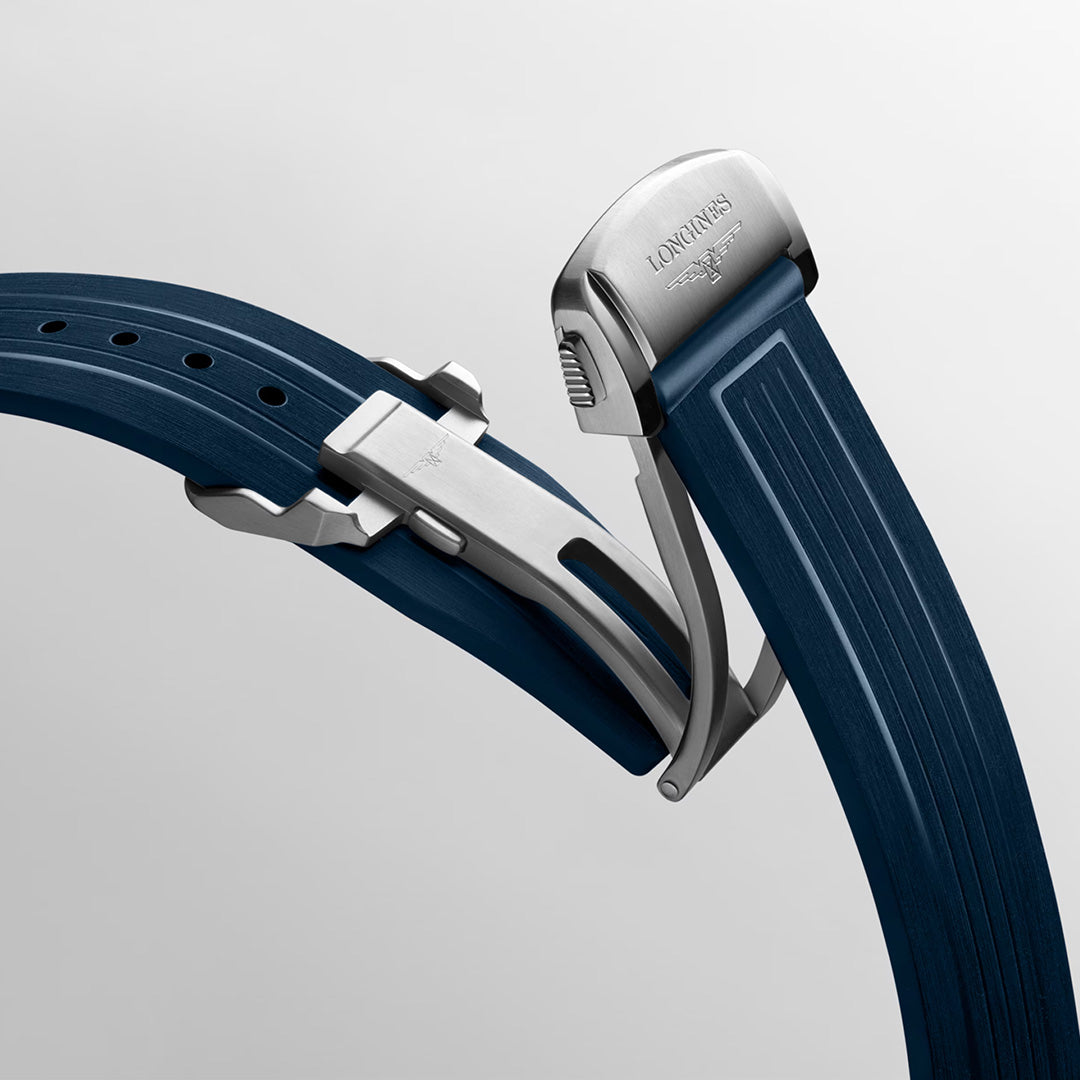 A close-up studio shot features the blue rubber strap of the Longines HydroConquest GMT Automatic 41mm Watch, highlighted by a partially open silver stainless steel deployment clasp. The clasp showcases the engraved Longines logo—a hallmark of this timepiece from the Longines Sport Collection. The watch is set against a clean, minimalist off-white background.