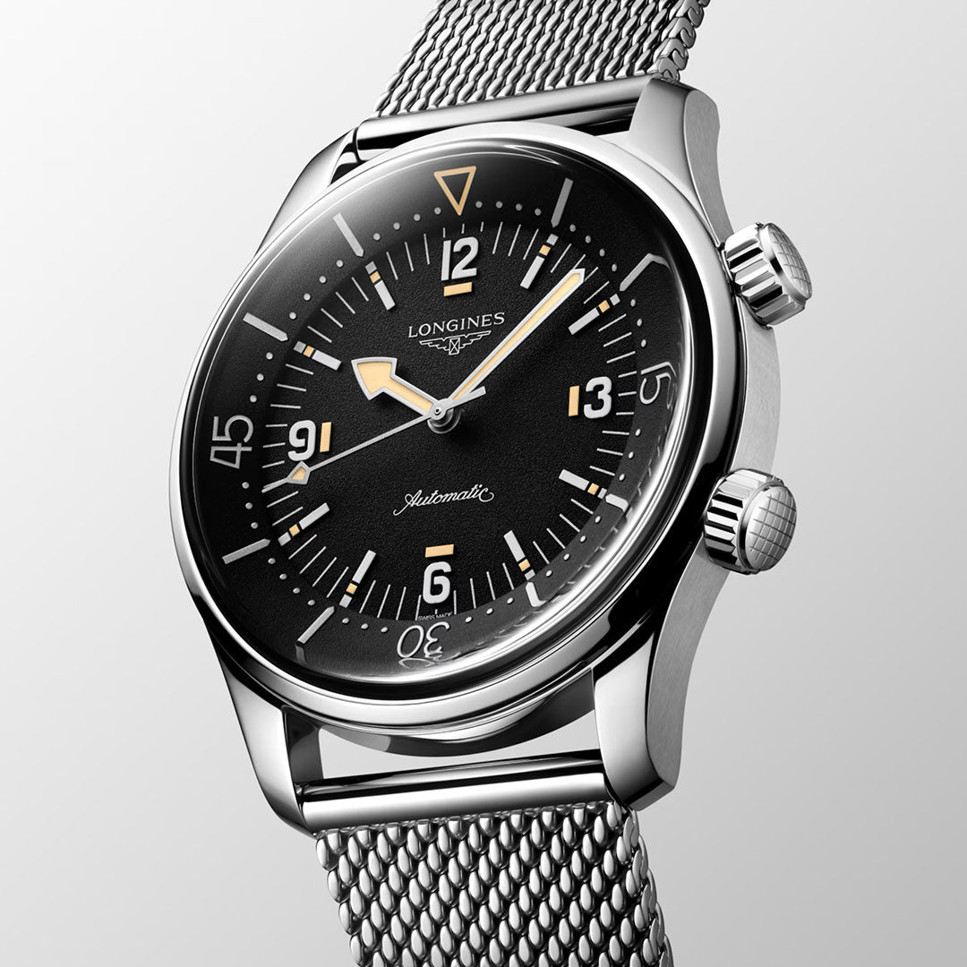 A close-up of the Longines Legend Diver 59 Automatic 42mm Watch with a black dial, bold white markers with Swiss Super-Luminova, yellow accents, dual crowns, and a stainless steel mesh strap, displayed at an angle on a light background.